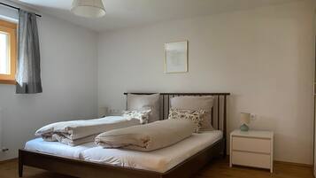 Un letto matrimoniale con struttura in legno e due cuscini, un comodino con una lampada, e una finestra con tenda.