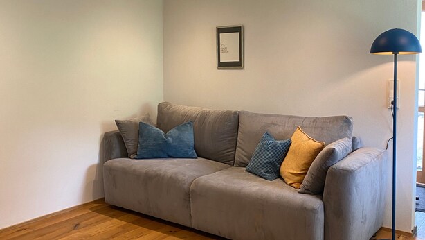 Un salón con sofá gris, suelo de madera, luces empotradas en el techo y una lámpara de pie.