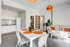 A modern kitchen with white cabinets and a dining area with a white table and grey chairs. - FaMa | Quiet&Bright 2-Bedroom Apartment (Roma)