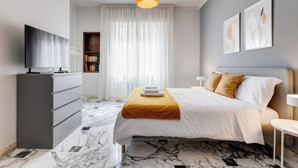 Et moderne hotelværelse med en seng, et fjernsyn, en bogreol og et stort vindue med gardiner.