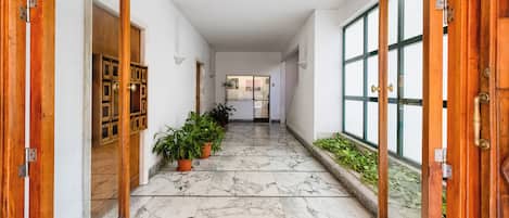 Un pasillo con suelo de mármol, puertas de madera y plantas en macetas.