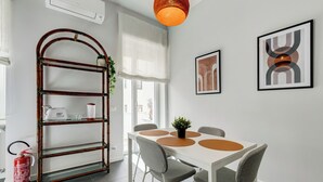 Et moderne spiseområde med et hvidt bord, grå stole og en træbogreol.