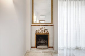 Ein Zimmer mit Kamin, einem großen Spiegel und einem Fenster mit durchsichtigen Vorhängen.