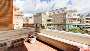En balkon med en potteplante, en træbænk og udsigt til høje bygninger.