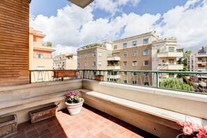 Ein Balkon mit einem Blumentopf, einer Holzbank und Blick auf mehrstöckige Gebäude.