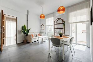 A modern living space with a dining area, a sofa set, a potted plant, and a large window. - FaMa | Quiet&Bright 2-Bedroom Apartment (Roma)