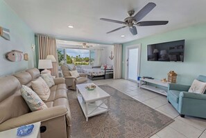 A spacious living room with a sofa, coffee table, and a television. - Steps to Sapphire's Sandy Beach - D12 Crystal Cove - Sapphire Bay West (St Thomas)