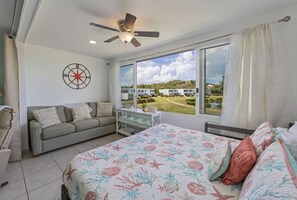 Ein Schlafzimmer mit Bett, einer Couch, einem Schreibtisch und einem großen Fenster mit Blick auf Häuser.