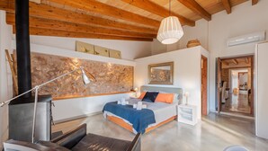 Un dormitorio moderno con pared de piedra, cama con ropa de cama azul y naranja, techo de madera y mesita de noche blanca.