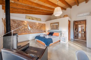 A modern bedroom with a stone wall, a bed with blue and orange bedding, a wooden ceiling, and a white bedside table. - Villa Near Pollenca Town Centre (Pollença)