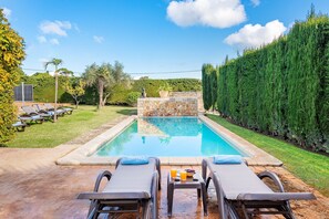 A rectangular swimming pool with a stone wall in the center, surrounded by a well-maintained lawn and a tall hedge. - Villa Near Pollenca Town Centre (Pollença)