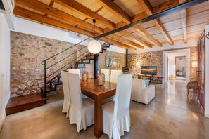 A spacious living area with a wooden ceiling, stone walls, a staircase, and a dining table with chairs. - Villa Near Pollenca Town Centre (Pollença)