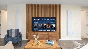 A modern living room with a flat-screen TV displaying a movie selection menu, a wooden coffee table with decorative items, and a blue armchair. - Luxury 2BR Corner Apartment I Manchester I City (Greater Manchester)