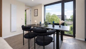 A modern dining area with a dark table, black chairs, and a view of greenery and buildings through large windows. - Luxury 2BR Corner Apartment I Manchester I City (Greater Manchester)