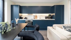 A modern kitchen with dark blue cabinets, a central island with seating, and a built-in oven. - Luxury 2BR Corner Apartment I Manchester I City (Greater Manchester)