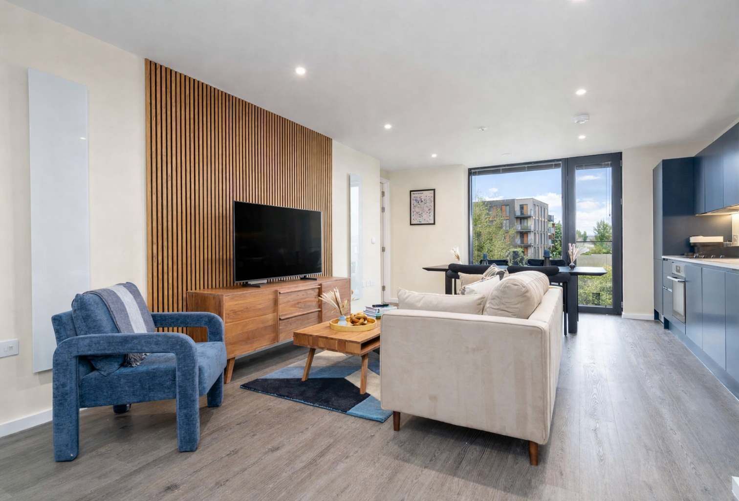A modern living room with a flat-screen TV, a sofa, a blue armchair, and a wooden accent wall.