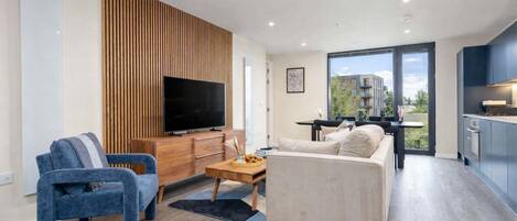 A modern living room with a flat-screen TV, a sofa, a blue armchair, and a wooden accent wall.
