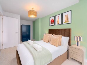 Ein Hotelzimmer mit einem Bett, einem Nachttisch, einer Lampe, einem Kleiderschrank und drei gerahmten Bildern an der Wand.