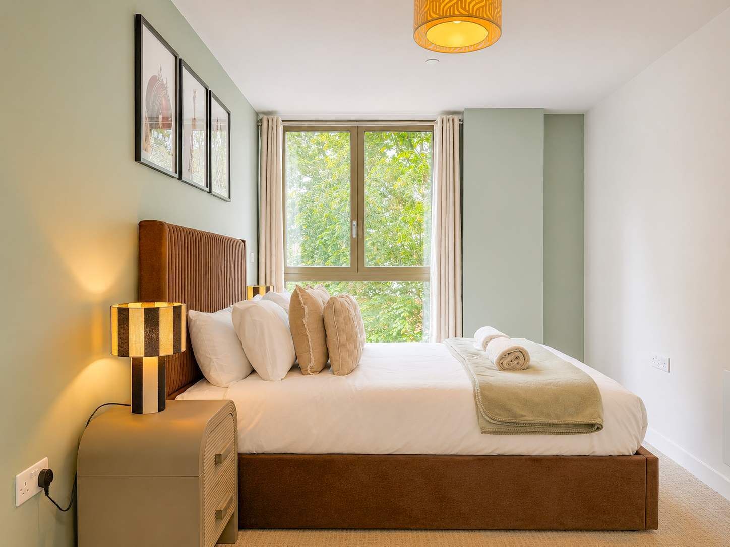 Ein Schlafzimmer mit Bett, Nachttischlampe, Fenster und einem Bild an der Wand.