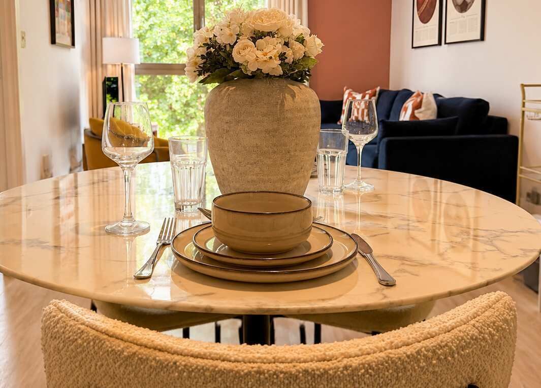 Mesa redonda para refeições com um vaso de flores, uma tigela e talheres.