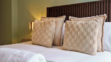 Quarto de hotel com cama, duas almofadas, cabeceira e uma luminária fixada na parede.