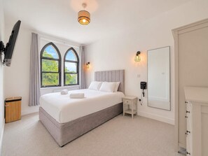 Ein Schlafzimmer mit einem großen Bett, einem an der Wand befestigten Fernseher, einem Nachttisch und einem Fenster mit Vorhängen.
