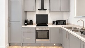 A modern kitchen with grey cabinets, a black stove, a microwave, and a sink. - Beautiful House 2BR - Sleeps 6 - Free Parking - Huddersfield (Huddersfield)