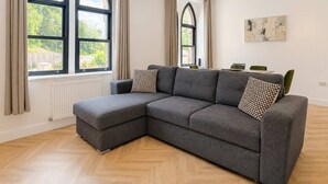 A modern living room with a sectional sofa, large windows, and a dining area. - Beautiful House 2BR - Sleeps 6 - Free Parking - Huddersfield (Huddersfield)