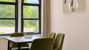 A dining area with a table and chairs, large arched windows, and a painting on the wall. - Beautiful House 2BR - Sleeps 6 - Free Parking - Huddersfield (Huddersfield)