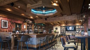 A bar area with wooden bar counters, bar stools, and a variety of bottles and glasses. - Hotel Bergkristall Zillertal-Adults Only (Hippach)