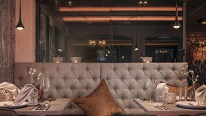 A dining area with a tufted bench, table set with glassware, and pendant lighting. - Hotel Bergkristall Zillertal-Adults Only (Hippach)