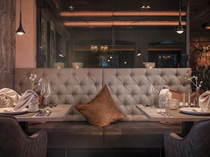 A dining area with a tufted bench, table set with glassware, and pendant lighting.