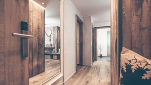 A hallway with wooden flooring, a mirror, and a door leading to a room with a bed and a decorative wall piece. - Hotel Bergkristall Zillertal-Adults Only (Hippach)