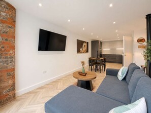 Ein modernes Wohnzimmer mit grauem Sofa, einem kleinen runden Tisch und einem flachbildfernseher an der Wand.