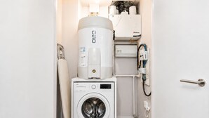 Une petite buanderie équipée d’un lave-linge à chargement frontal, d’un chauffe-eau et d’un radiateur fixé au mur.