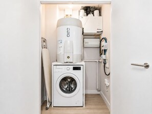 Ein kleiner Hauswirtschaftsraum mit einer Waschmaschine mit Frontlader, einem Warmwasserbereiter und einem Wandheizkörper.