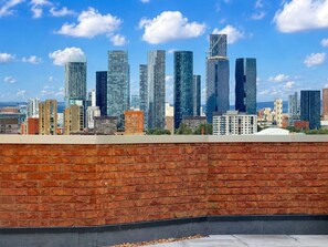 Eine Stadtlandschaft mit modernen Hochhäusern, einer Backsteinmauer im Vordergrund und einem klaren, blauen Himmel.