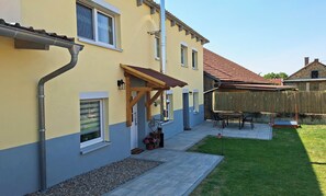 A residential building with a tiled patio, a wooden pergola, and a fenced backyard.