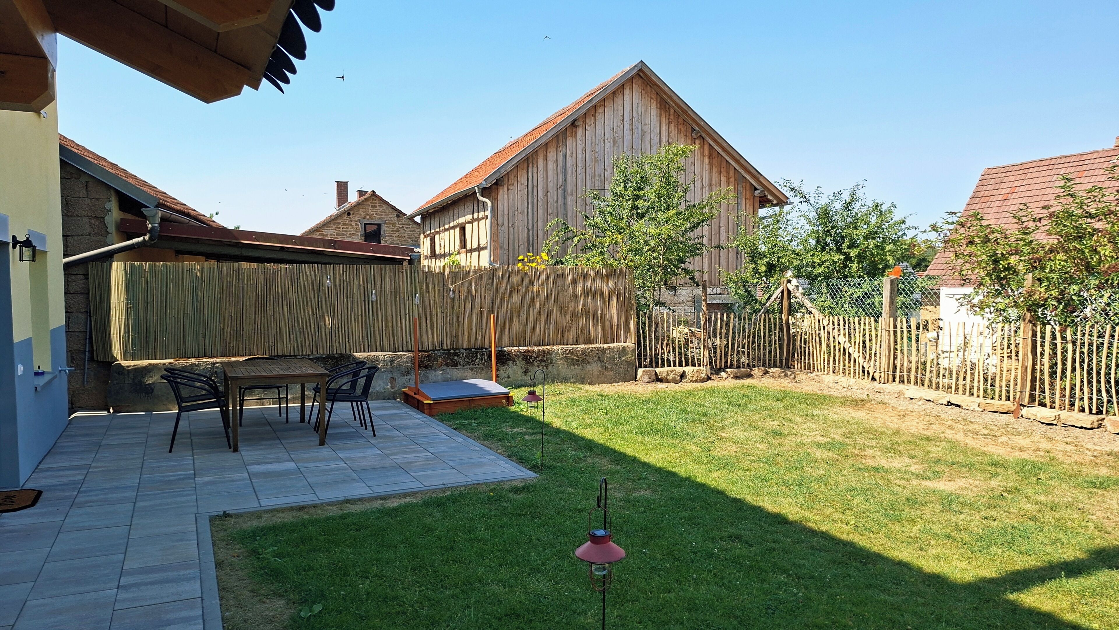 Un jardin avec une table et des chaises en bois, un petit potager et une clôture en bois.