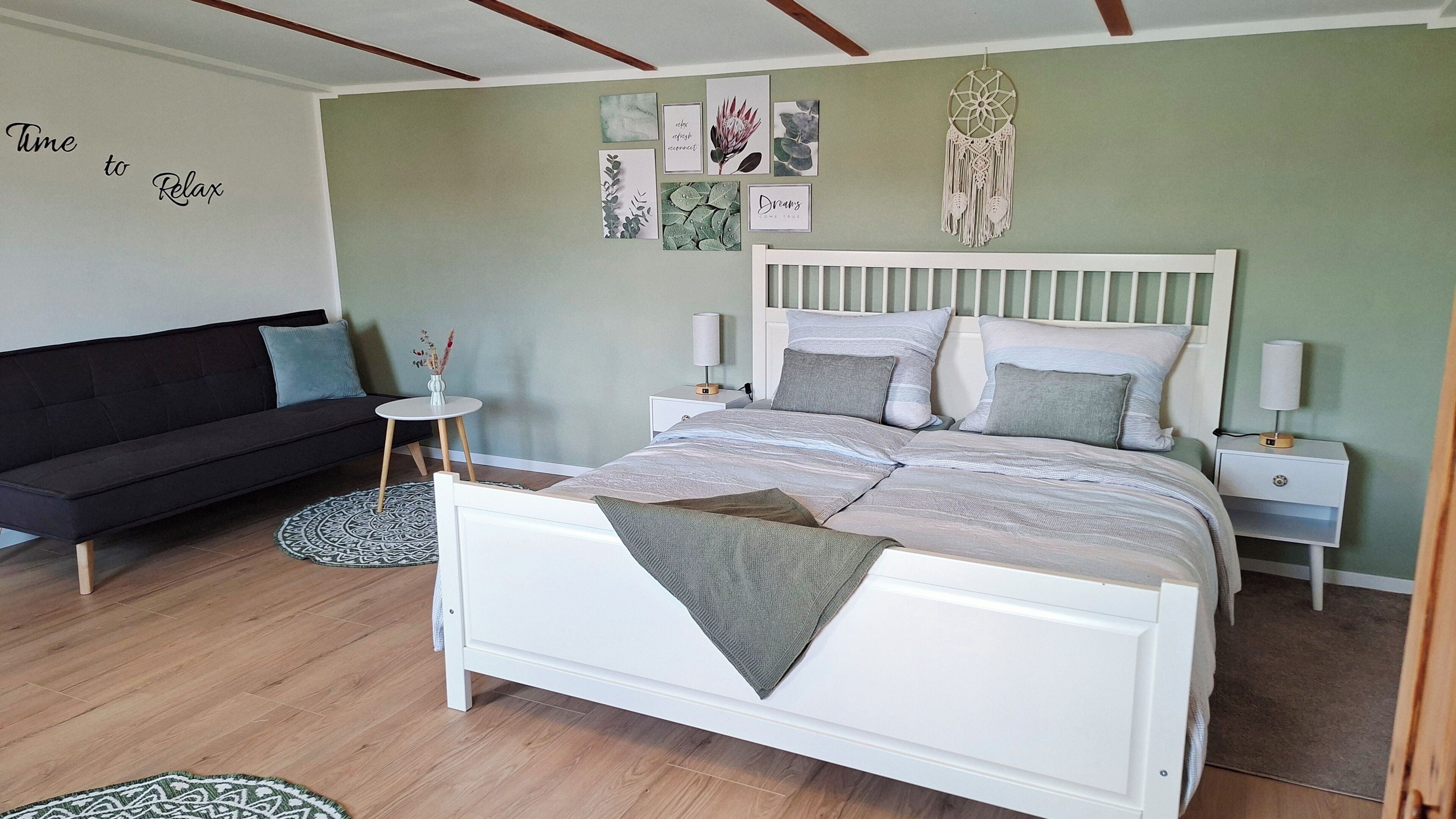 Ein Schlafzimmer mit einem weißen Bett, grauen Kissen, einem kleinen Nachttisch mit Lampe und einer Wand mit gerahmten Bildern.