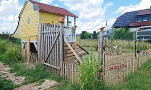 A yellow house with a wooden gate, a solar panel on the roof, and a fenced area with plants and a bird feeder.