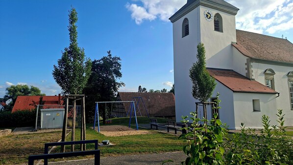 A church with a bell tower, a playground with swings, and a small building with a red roof.