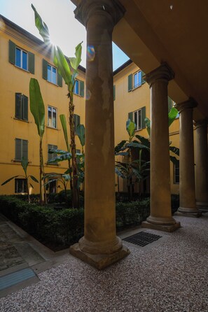 Ein Innenhof mit Säulen, ein gelbes Gebäude und grüne Fensterläden.