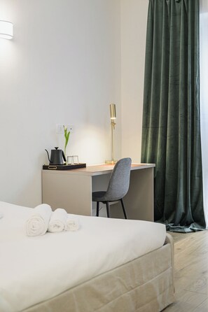 A hotel room with a bed, a desk, a chair, a lamp, and a curtain. - Bologna Historic Center: Spacious 4-Bedroom, 4-Bathroom Home (Bologna)