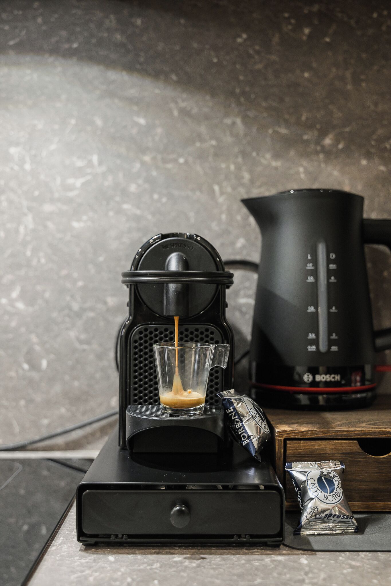Eine Kaffeemaschine mit Glasbehälter auf einem Tisch, eine Kaffeekanne und ein Kaffeepäckchen.