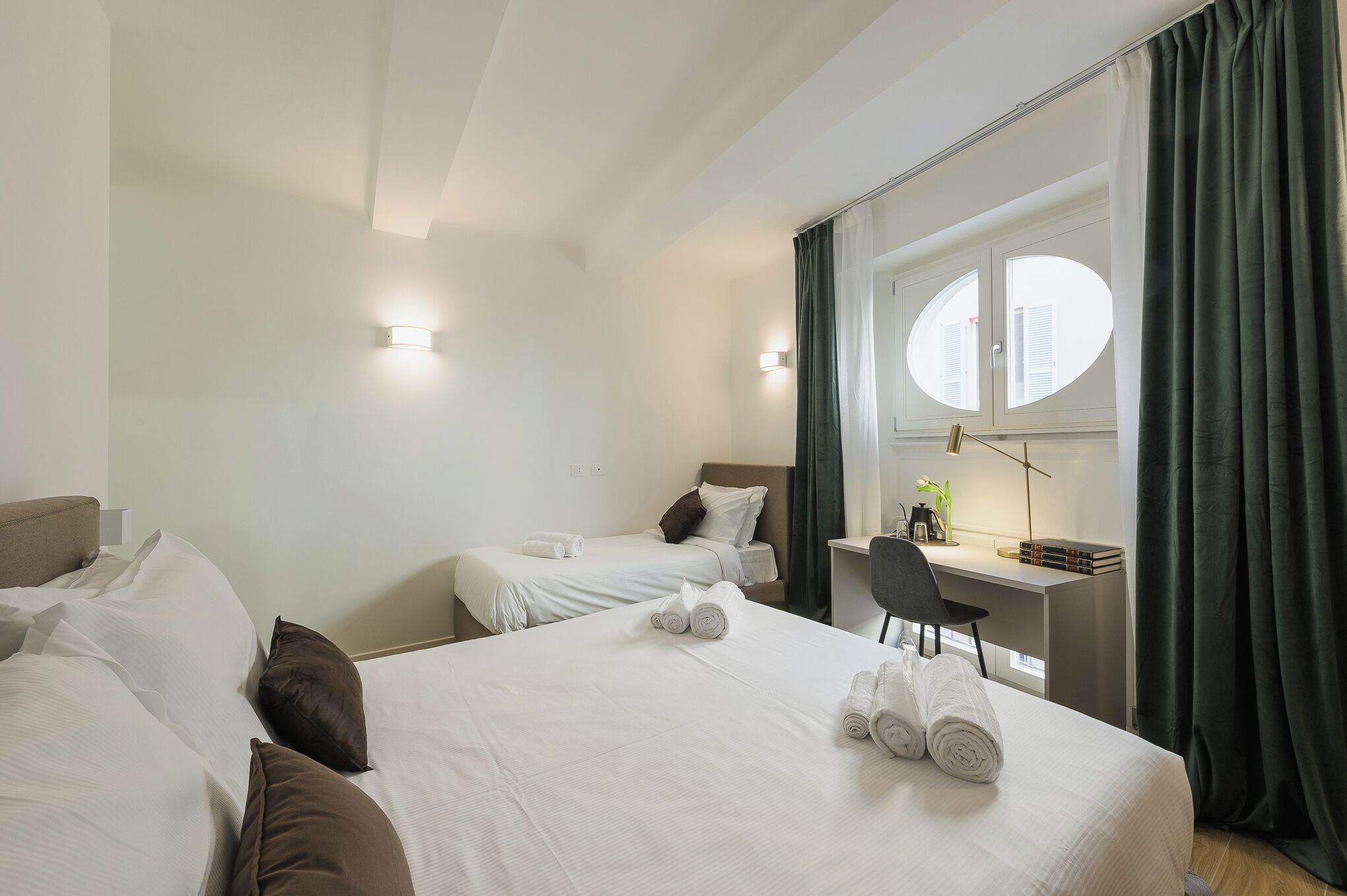 Habitación de hotel con dos camas, un escritorio, una silla y un ventanal con cortinas.