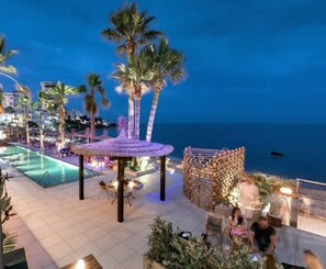 A resort pool area with a thatched gazebo, palm trees, and a view of the ocean. - 
Exclusive semi-detached house, at short distance from the beach and local shops (Calahonda)