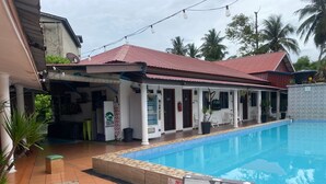 A swimming pool with a tiled deck, a covered outdoor seating area, and a building with a red roof. - Hotel O Panggas Village Homestay (Kangar)