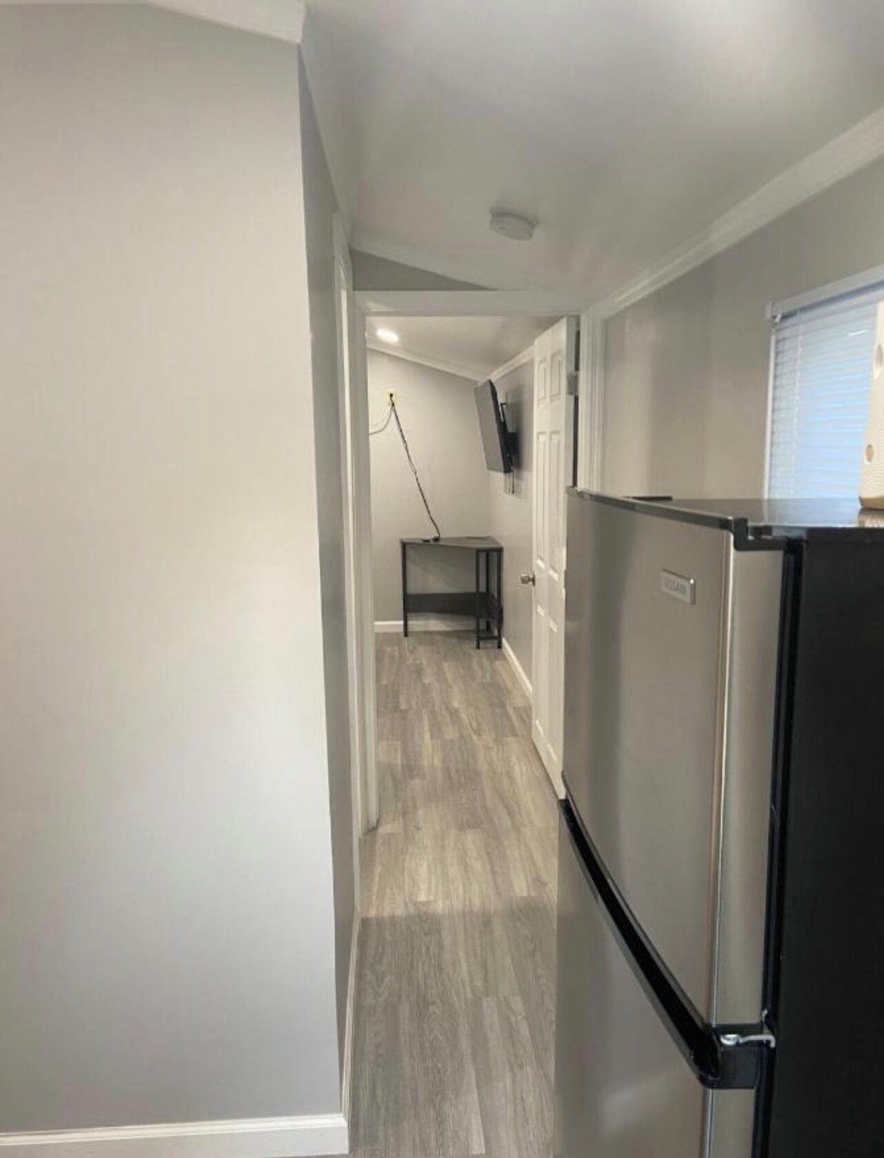 A narrow hallway with a refrigerator and a television mounted on the wall.