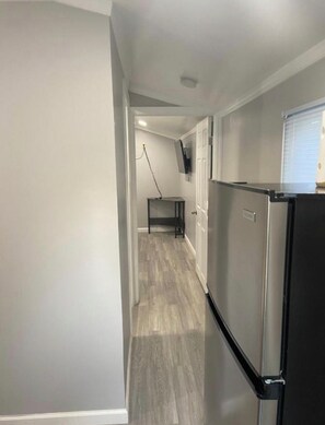 Un pasillo estrecho, con un refrigerador a la derecha y un televisor colgado en la pared.